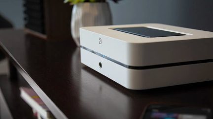 Lille mat hvidt rektangulært plastikkabinet med en central blank sort stribe, frontvendt 3,5 mm jackstik og indfældet sort touchpad på toppen, set fra højre forperspektiv