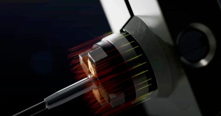 Vue rapprochée d'un connecteur métallique cylindrique avec des lignes lumineuses rouges et jaunes, fixé à une structure grise angulaire