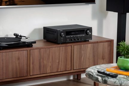 Amplificateur audio noir sur meuble en bois, platine vinyle noire à côté, plante verte derrière