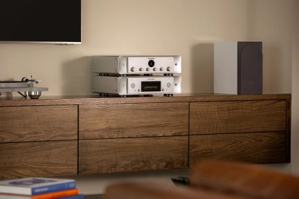 Meuble en bois avec deux amplificateurs hi-fi argentés posés dessus, un haut-parleur noir à droite