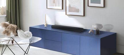 Blue rectangular low cabinet with 6 compartments, black soundbar, glass lamp, beige candle holder, glass coffee table