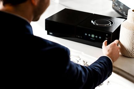 Homme en costume ajustant un appareil électronique noir rectangulaire avec boutons, posé sur une surface blanche