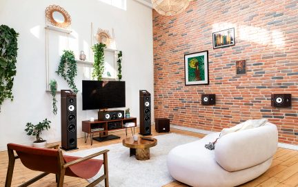 Salon avec mur en briques, canapé blanc, fauteuil en bois, table basse ronde, télévision, enceintes, plantes et décorations murales