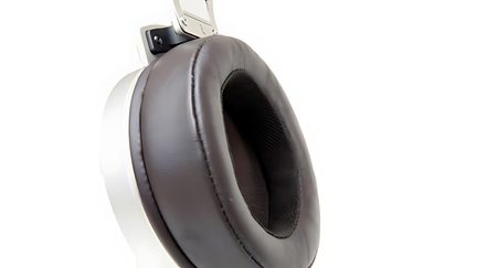 Primo piano di un padiglione auricolare di cuffie in similpelle marrone, interno in rete nera, struttura in plastica bianca, vista angolata