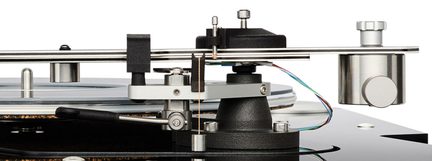 Gros plan latéral sur un bras de lecture de platine vinyle en métal argenté fixé sur base noire texturée, avec contrepoids cylindrique assorti et fins câbles multicolores apparents