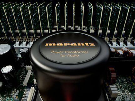 Vue rapprochée d'un transformateur cylindrique noir avec texte doré, entouré de circuits imprimés, condensateurs et dissipateurs