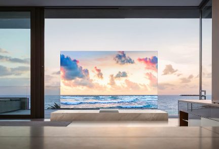 Téléviseur affichant un coucher de soleil sur l'océan avec des nuages colorés, dans une pièce avec de grandes fenêtres