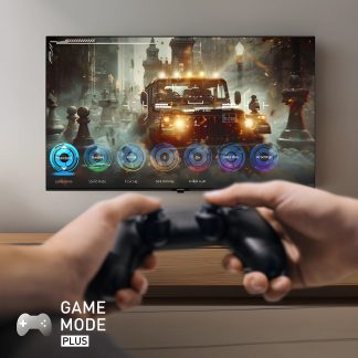 Écran plat mural affichant un jeu vidéo avec véhicule, mains tenant une manette noire au premier plan, texte "Game Mode Plus"