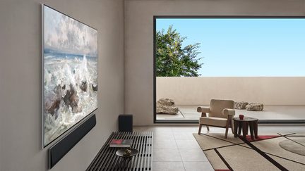 Téléviseur mural ultra plat argenté à cadre métallique et surface en verre affichant une peinture marine, vue en légère perspective latérale gauche