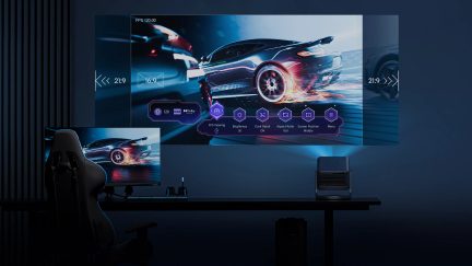 Salle sombre, écran géant avec voiture en mouvement, projecteur sur table, chaise gaming, écran d'ordinateur, clavier
