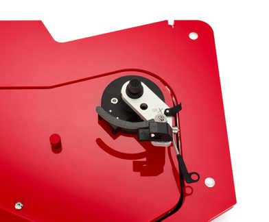 Gros plan vue de dessus d’un tourne-disque à surface rouge brillante en acrylique, doté d’un pivot de bras de lecture argenté et noir et d’un petit bouton cylindrique rouge