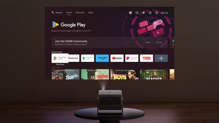 Un projecteur sur une table projette une interface Google Play avec des icônes d'applications et des images de contenu sur un mur