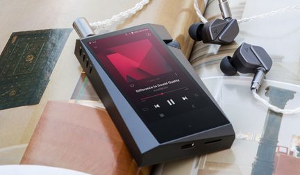 Baladeur numérique noir posé sur livre ouvert, avec écouteurs intra-auriculaires gris et argentés à côté