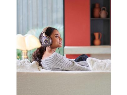 Jeune femme assise sur un canapé blanc, portant un pull gris, écoutant de la musique avec un casque audio argenté