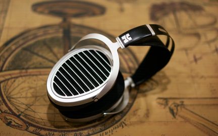 Un casque audio argenté avec des oreillettes ovales à grilles noires et un arceau noir posé sur une surface beige avec motifs