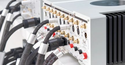 Vue arrière d'un amplificateur audio avec connecteurs RCA dorés, XLR noirs, borniers rouges et noirs, câbles gainés noirs