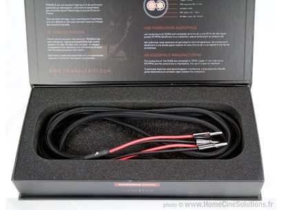 Câble audio noir avec connecteurs rouges, enroulé dans un boîtier rectangulaire noir, sur une brochure grise