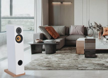 White floor-standing speaker with a wooden base, gray sectional sofa with orange and gray cushions, black and marble coffee tables