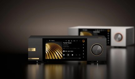 En sort audioapparat med en central skærm, der viser musikoplysninger, en gylden cirkulær knap til højre, sløret baggrund.