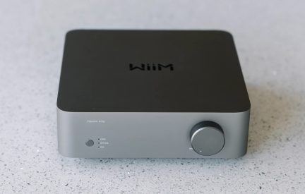 Rektangulärt grått hölje med svart ovansida, cirkulär knapp till höger, texten "Wiim" på ovansidan och "Vibelink Amp" längst ner till vänster