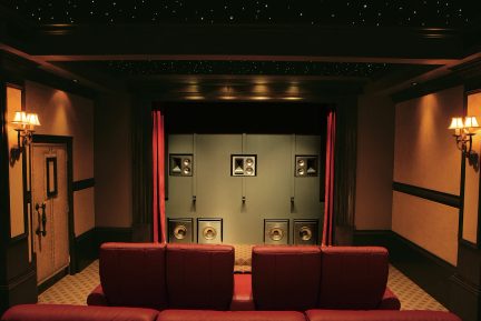 Salle de cinéma privée avec sièges en cuir rouge, mur de haut-parleurs, rideaux rouges, plafond étoilé, appliques murales