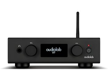 Vista frontale di un DAC Audiolab D7 nero in metallo, con chassis rettangolare poggiato su piedini, display centrale retroilluminato, due manopole rotonde, presa per cuffie, pulsante di accensione a LED e antenna verticale