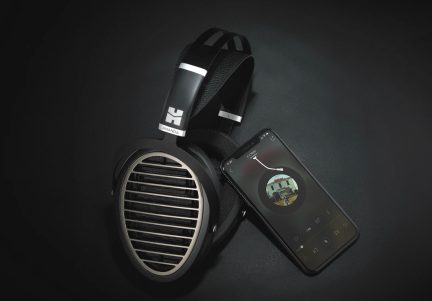 Un casque audio noir avec des grilles métalliques ovales et un smartphone affichant une interface de lecture musicale sur fond noir