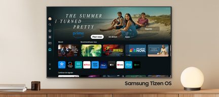 Téléviseur Samsung Tizen OS affichant l'interface utilisateur avec des applications de streaming, posé sur un meuble en bois clair avec une lampe sphérique blanche et des livres