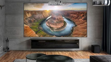 Écran mural rectangulaire avec image de canyon, meuble bas noir, projecteur suspendu, sol en bois, table ronde en verre