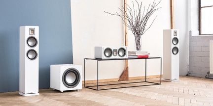 Zestaw audio składający się z dwóch kolumn podłogowych, głośnika centralnego i subwoofera, prostokątne obudowy z białego lakierowanego drewna z okrągłymi szarymi głośnikami i prostokątnymi wstęgowymi tweeterami, widok z przodu