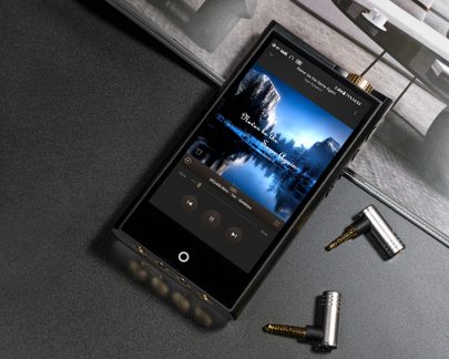 Black portable digital audio player in metal with large touchscreen display showing playback and a row of gold jack outputs at the bottom, top view at a slight angle