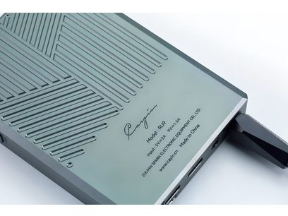 Baksida i lätt uppifrånperspektiv på den bärbara ljudomvandlaren Cayin RU9 i anodiserad grågrön aluminium, dekorerad med diagonalt frästa rännor och tryckta märkningar.