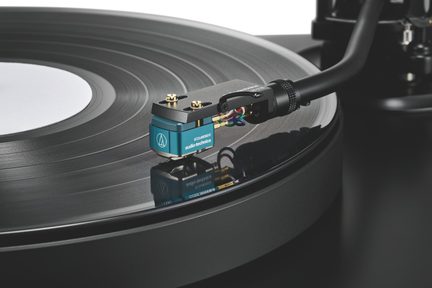 Testina fono blu in metallo su braccio di lettura nero, puntina sul vinile nero con solchi visibili, vista obliqua