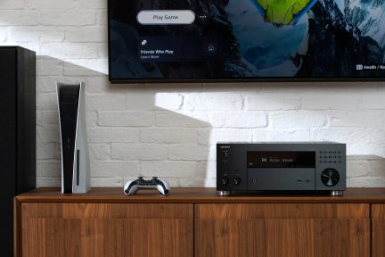 Vertical white console, two-tone controller, black amplifier, wall-mounted screen, white brick wall, wooden furniture