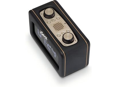 Roberts Revival Rest radio galda melnā ar graudainu mākslīgo ādu, zelta apmales, šampaņa krāsas augšējo paneļu ar diviem lieliem metāla rotējošiem pogām un centrālo skaļruņa režģi, frontālo ciparu displeju, trīs ceturtdaļu skatu no augšas un priekšas