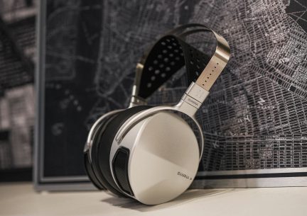Un casque audio argenté avec des coussinets noirs et un arceau perforé noir et beige posé devant une carte géographique noire et blanche