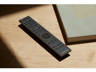 Télécommande noire Marantz avec touches numériques et de contrôle, posée sur une surface en bois clair près d'un livre ouvert