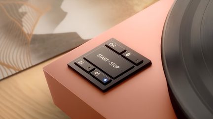 Płyta winylowa w kolorze koralowym, podstawa z matowym wykończeniem metalicznym, zbliżenie na przyciski START·STOP, 33/45, odtwarzanie, Bluetooth, niebieska dioda LED
