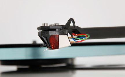 Vedere laterală a unei celule de pick-up pentru vinil cu corp negru, vârf argintiu, cabluri colorate, fundal neclar albastru și negru.
