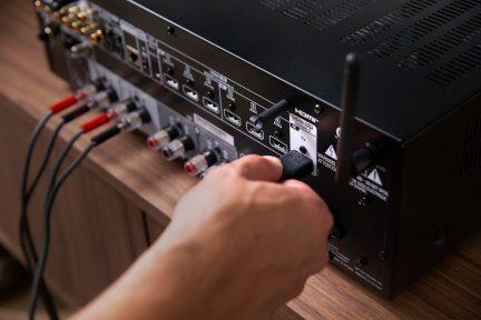 Main tenant un câble connecté à l'arrière d'un amplificateur audio noir avec plusieurs ports et boutons