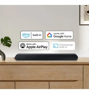 Rectangular black soundbar placed on a light wood cabinet, green plant on the left, compatibility icons displayed above.