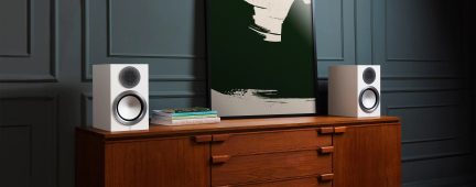 Deux enceintes blanches sur un meuble en bois avec tiroirs, tableau abstrait vert et blanc, livres empilés