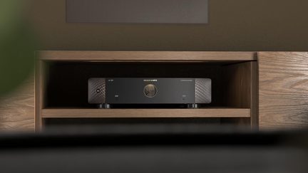 Black Marantz audio amplifier with smooth front panel in a light wood TV cabinet, front view