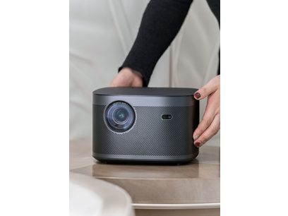 Μπροστινή όψη του μαύρου βιντεοπροβολέα XGIMI Horizon Pro 4K, φακός και αισθητήρας, χέρι που κρατάει το επάνω μέρος
