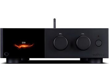 Audiolab D9 black metal audio DAC converter, front view, rectangular case on feet with glossy display on the left showing an orange pattern and the text D9, two large rotary selection and volume knobs in the center, power button and LED on the right, slim vertical antenna in the background