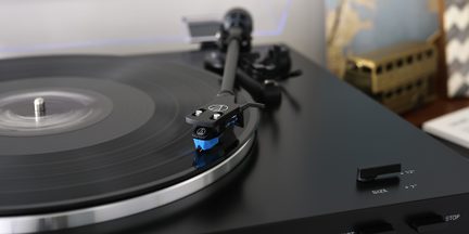 Une platine vinyle noire avec un disque noir, un bras de lecture avec une cellule bleue et un sélecteur de taille 12" ou 7"