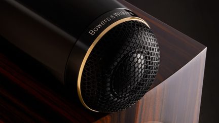 Haut-parleur noir et or de forme cylindrique, vue rapprochée de face, grille métallique en nid d'abeille, inscription "Bowers & Wilkins"