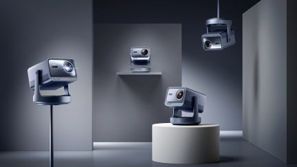 Quatre projecteurs gris, positions variées, sur socles et suspendus, dans une pièce aux murs gris, éclairage doux