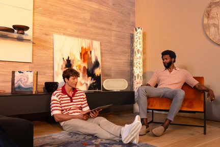 Cassa wireless beige posata sul mobile TV in un salotto moderno, due uomini seduti rilassati intorno