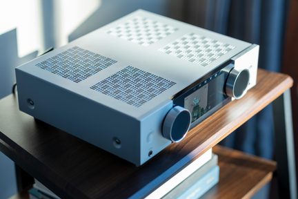 Srebrny wzmacniacz Hi‑Fi Onkyo z kolorowym wyświetlaczem z przodu i dwoma dużymi pokrętłami, ustawiony na drewnianej półce